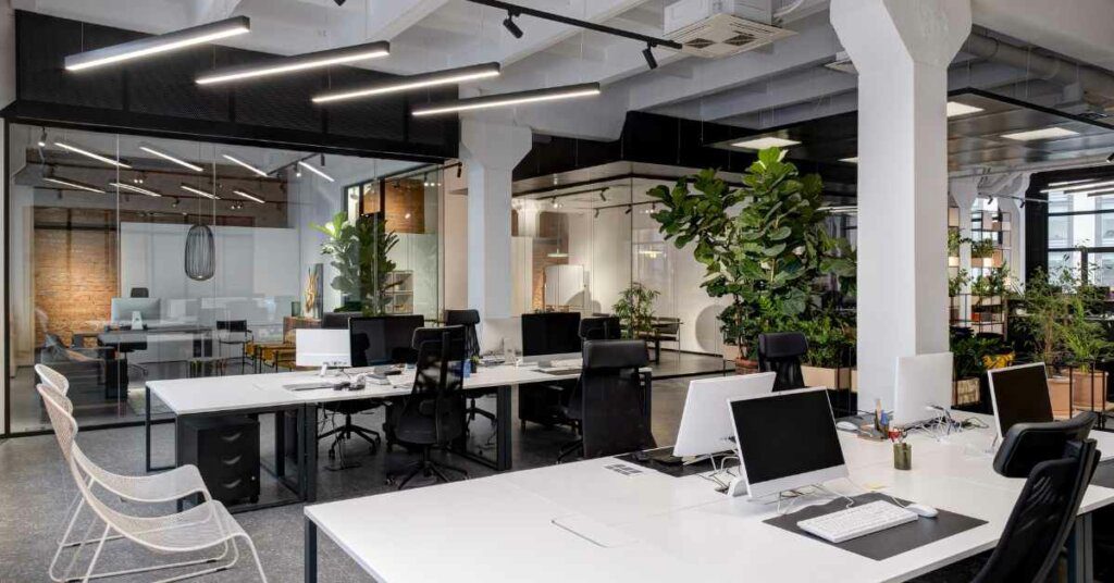kantor modern dengan meja berwarna putih yang terdapat laptop di atasnya dan tumbuhan di dalam ruangan Smart Office solusi kantor modern di Indonesia